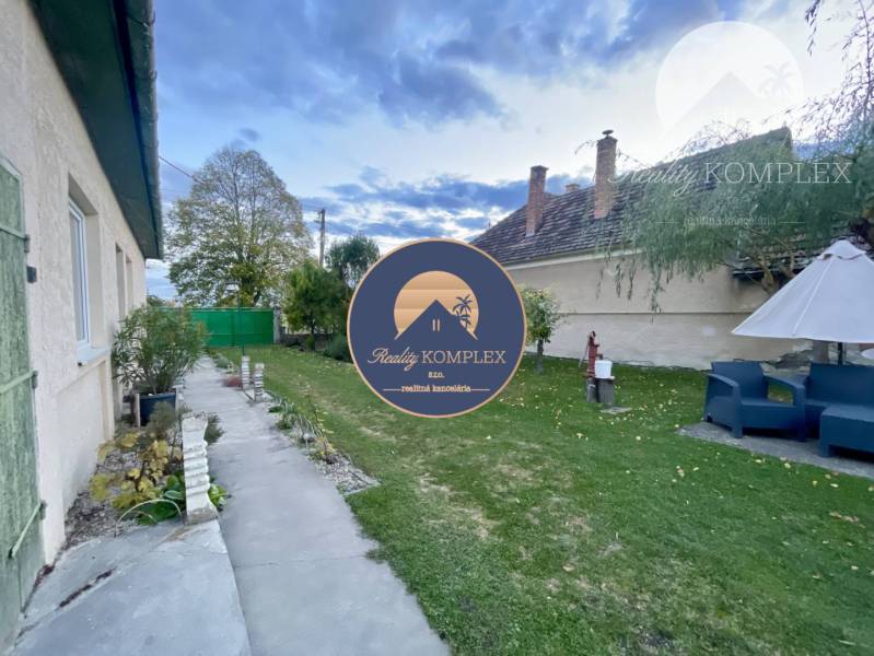 Investičný pozemok s obývateľným domom vo Vrakúni - Záhrada pri rodinnom dome vo Vrakúni s chodníkom, zeleňou a bielym slnečníkom.