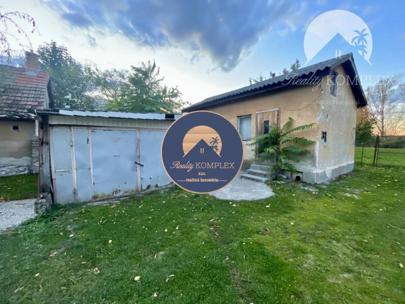 Investičný pozemok s obývateľným domom vo Vrakúni - Rodinný dom vo Vrakúni s plechovou prístavbou obklopený trávnikom a stromami.