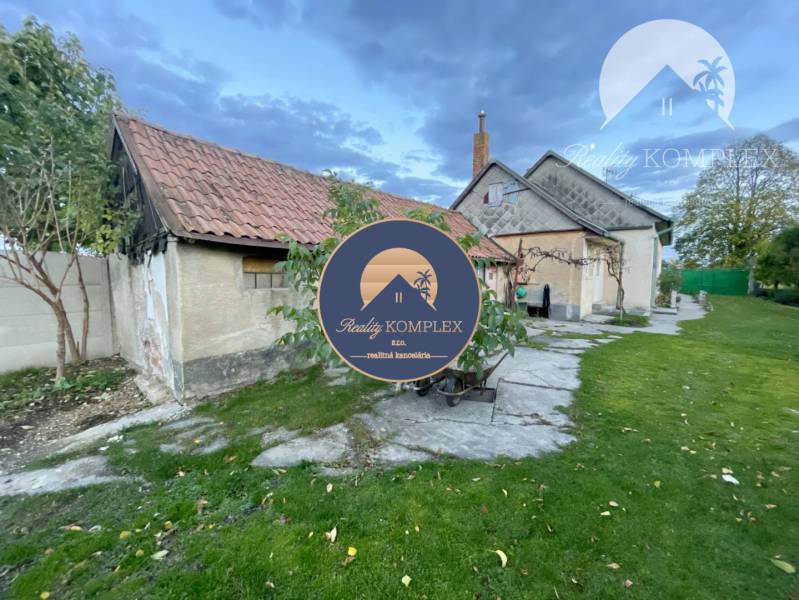 Investičný pozemok s obývateľným domom vo Vrakúni - Rodinný dom vo Vrakúni s trávnikom, stromami a prístavbou pod zamračenou oblohou.