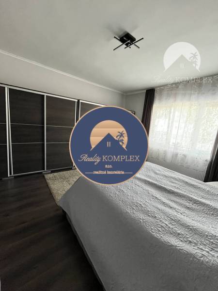 Vám ponuka na predaj útulný 3-izbový rodinný d - Spálňa v rodinnom dome s tmavou podlahou s dreveným dekorom a veľkou skriňou.