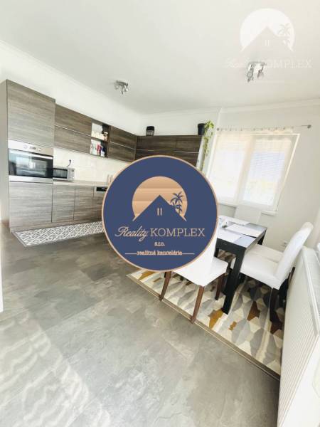 Vám ponuka na predaj útulný 3-izbový rodinný d - Kuchyňa v rodinnom dome s podlahou s dreveným dekorom, jedálenským stolom a veľkým oknom.