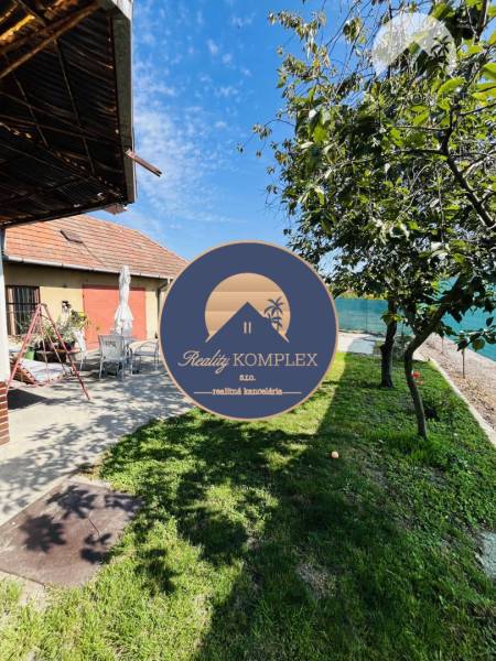 Vám ponuka na predaj útulný 3-izbový rodinný d - Exteriér rodinného domu vo Veľkom Mederi s trávnikom, stromami a terasou.