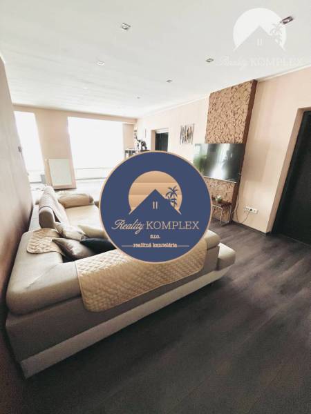 Vám ponuka na predaj útulný 3-izbový rodinný d - Obývacia izba v rodinnom dome s veľkou sedačkou a podlahou s dreveným dekorom.