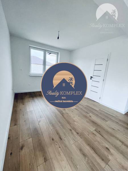 Vám ponúka na predaj moderný 4-izbový bungalov - Izba s bielymi stenami a podlahou s dreveným dekorom v rodinnom dome.