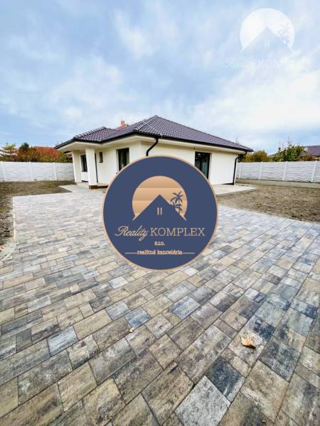 Vám ponúka na predaj moderný 4-izbový bungalov - Rodinný dom v Topoľníkoch so spevnenou plochou a strechou s tmavými škridlami.