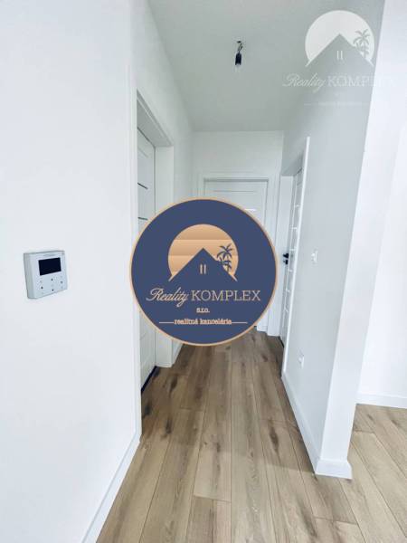 Vám ponúka na predaj moderný 4-izbový bungalov - Interiér rodinného domu s podlahou s dreveným dekorom a bielymi dverami.