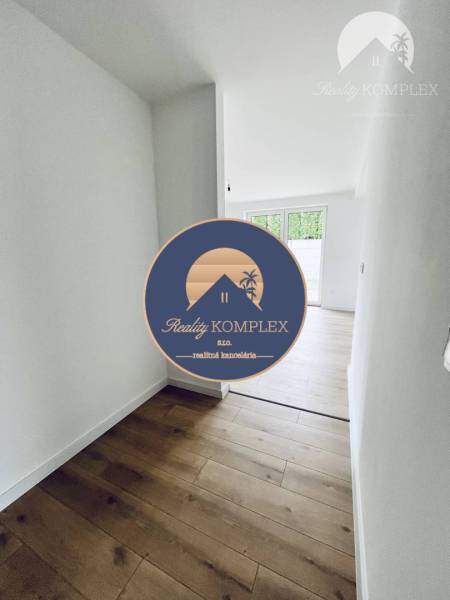 Vám ponúka na predaj moderný 4-izbový bungalov - Interiér rodinného domu s podlahou s dreveným dekorom a bielymi stenami.