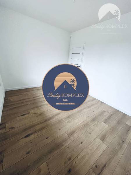 Vám ponúka na predaj moderný 4-izbový bungalov - Izba v rodinnom dome s bielymi stenami a podlahou s dreveným dekorom.