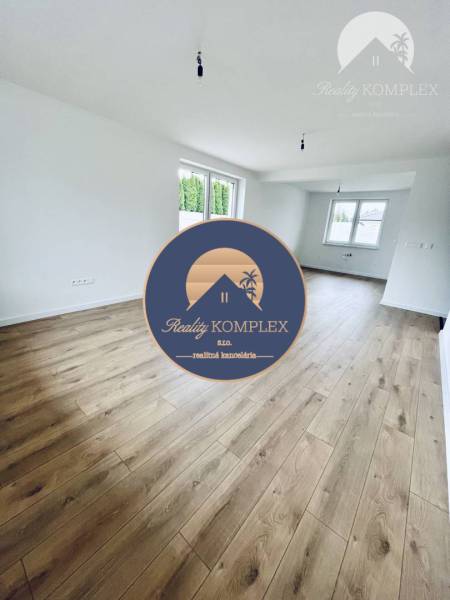 Vám ponúka na predaj moderný 4-izbový bungalov - Obývacia izba v rodinnom dome s podlahou s dreveným dekorom a veľkými oknami.