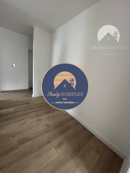 Vám ponúka na predaj moderný 4-izbový bungalov - Interiér rodinného domu s podlahou s dreveným dekorom a bielymi stenami.