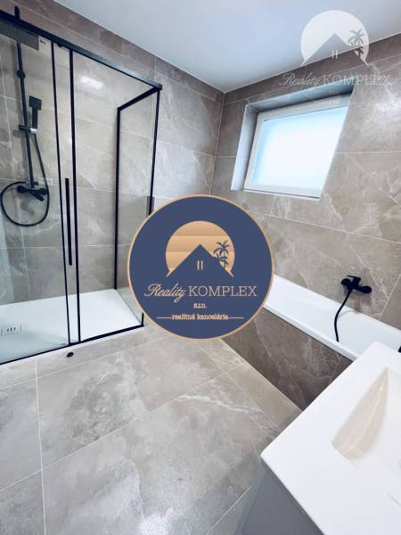 Vám ponúka na predaj moderný 4-izbový bungalov - Kúpeľňa v rodinnom dome s presklenným sprchovým kútom a svetlými obkladmi.