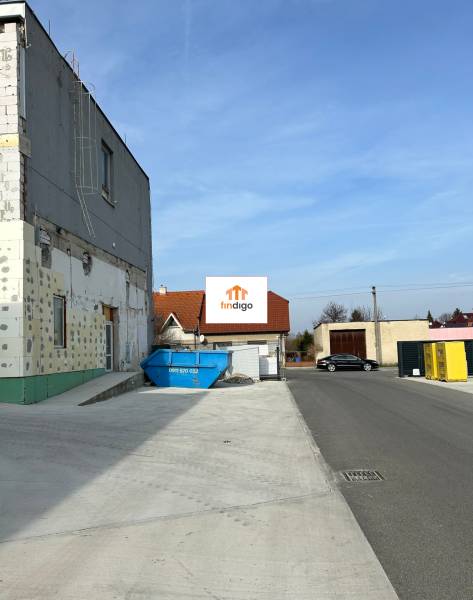 Autoservis s výbavou pre vozidlá v uzavretom priemyselnom areáli - HC - Budova v Hlohovci s kontajnerom a zaparkovaným autom na ulici.