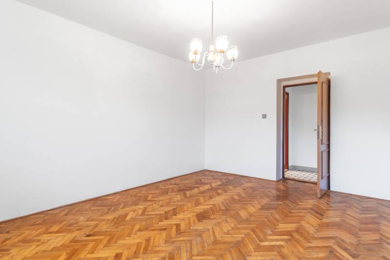 I Na predaj dvojposchodový 5i rodinný dom pri Žiline - Priestranná izba s podlahou s dreveným dekorom, lustrom a otvorenými dverami v rodinnom dome.