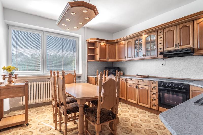 I Na predaj dvojposchodový 5i rodinný dom pri Žiline - Kuchyňa v rodinnom dome s drevenými skrinkami a jedálenským stolom, podlaha s dekorom.