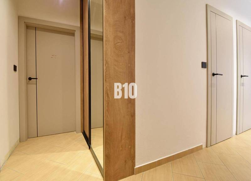 Veľkometrážny 3 izbový byt s garážou - Chodba v 3-izbovom byte s podlahou s dreveným dekorom a zrkadlovou skriňou.