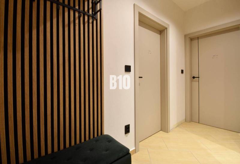 Veľkometrážny 3 izbový byt s garážou - Interiérová chodba s drevodekorom, dvomi dverami a podlahou s svetlým obkladom.