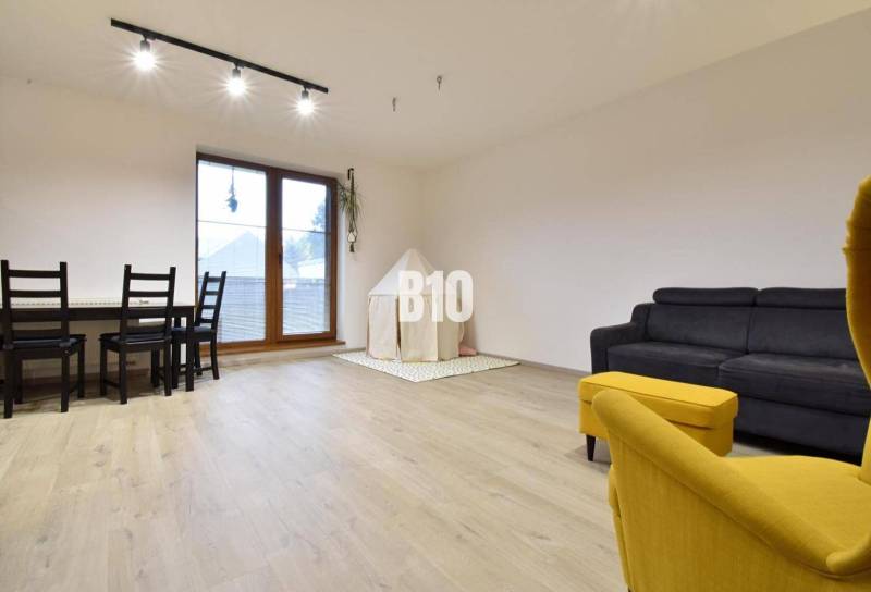 Veľkometrážny 3 izbový byt s garážou - Obývačka v 3-izbovom byte s podlahou s dreveným dekorom a žltým kreslom.