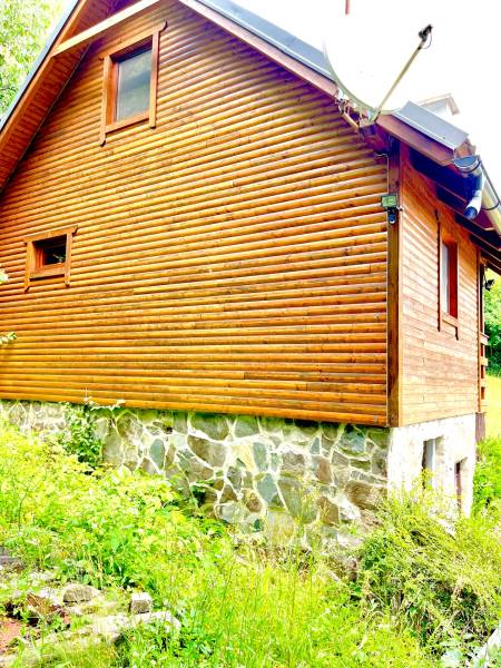 Rekreačná chata – Banská Štiavnica, časť Štefultov - Drevený rodinný dom v Štefultove s kamennou základňou obklopený zeleňou.