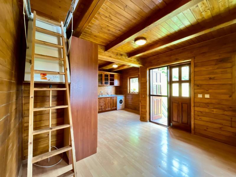 Rekreačná chata – Banská Štiavnica, časť Štefultov - Interiér rodinného domu s drevenými stenami, podlahou, kuchynskou linkou a schodmi na poschodie.