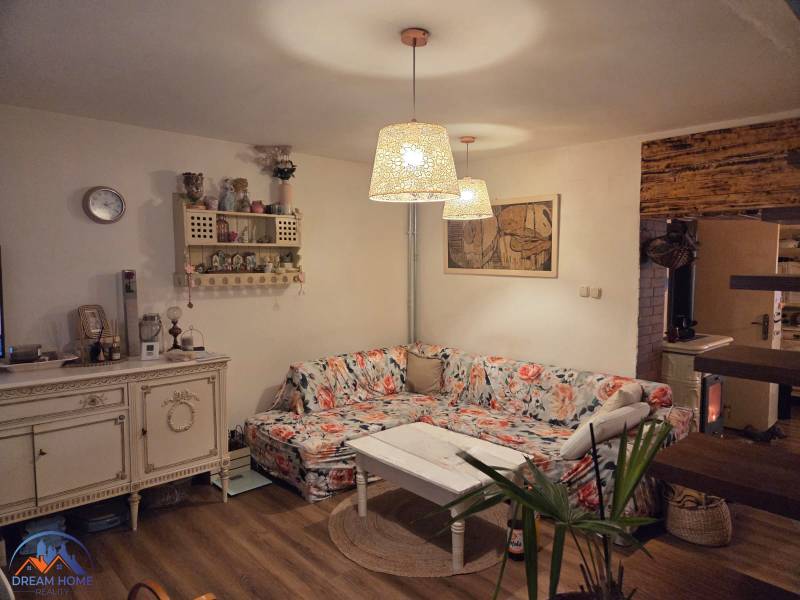 MH283 – Na predaj krásny rodinný dom vo vidieckom štýle - Rodinný dom, útulná obývačka, kvetinový gauč, dekoračné police, podlaha s dreveným dekorom.