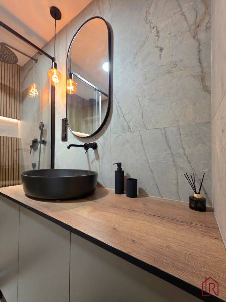 REZERVOVANÝ - Moderný 3-izbový byt po rekonštrukcii na Terase, Košice - Kúpeľňa v 3-izbovom byte s tmavou umývadlovou misou a podlahou s dreveným dekorom.