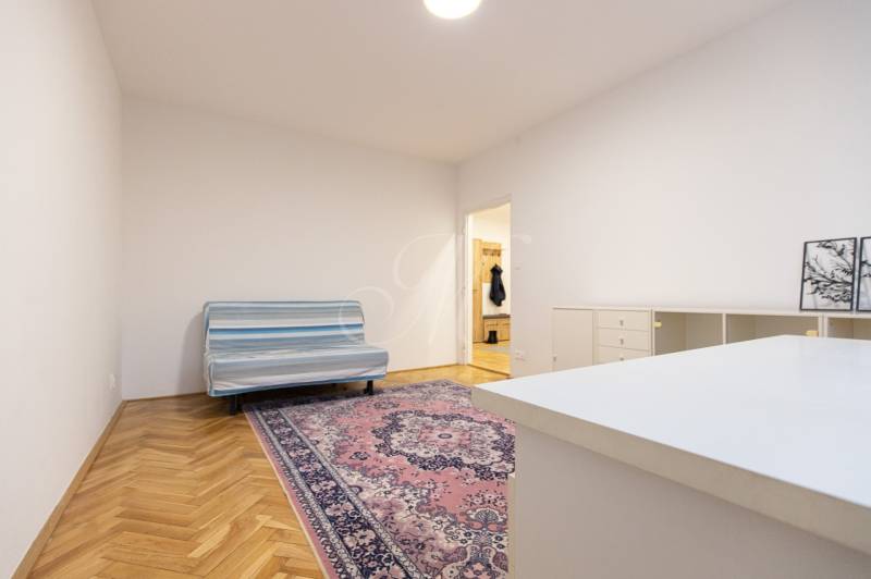 Slnečný 3-izbový byt, Kramáre - Izba v 3-izbovom byte s pohovkou, orientálnym kobercom a podlahou s dreveným dekorom.