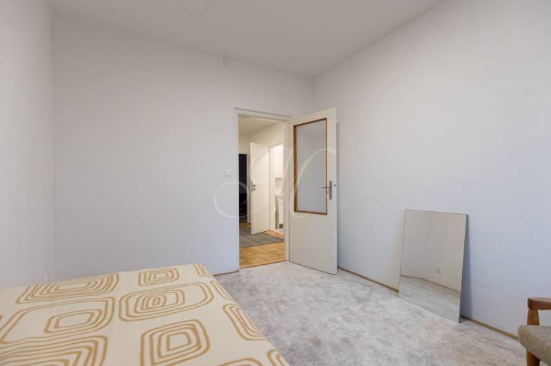 Slnečný 3-izbový byt, Kramáre - Biela izba s otvorenými dverami, koberec, zrkadlo a posteľná prikrývka v 3-izbovom byte.