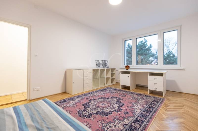 Slnečný 3-izbový byt, Kramáre - Spálňa v 3-izbovom byte s písacím stolom, kobercom a podlahou s dreveným dekorom.