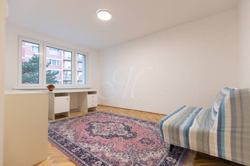 Slnečný 3-izbový byt, Kramáre - Izba s podlahou s dreveným dekorom, kobercom, stolíkom a pohovkou v 3-izbovom byte.