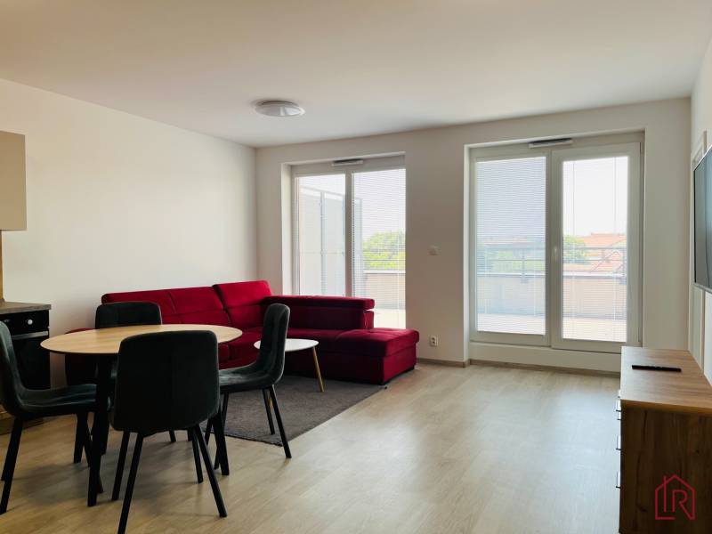 Prenájom, 3 izb.byt s terasou pri mestskom parku s park. miestom - Obývacia izba v 3-izbovom byte s podlahou s dreveným dekorom a červenou sedačkou.