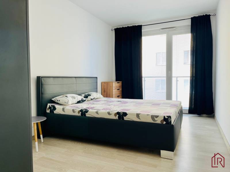 Prenájom, 3 izb.byt s terasou pri mestskom parku s park. miestom - Spálňa v 3-izbovom byte s posteľou, nočnými stolíkmi a podlahou s dreveným dekorom.