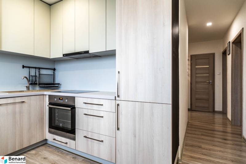 Útulný 2-izbový byt na prenájom - Kuchyňa v 2-izbovom byte s podlahou s dreveným dekorom a svetlými skrinkami.