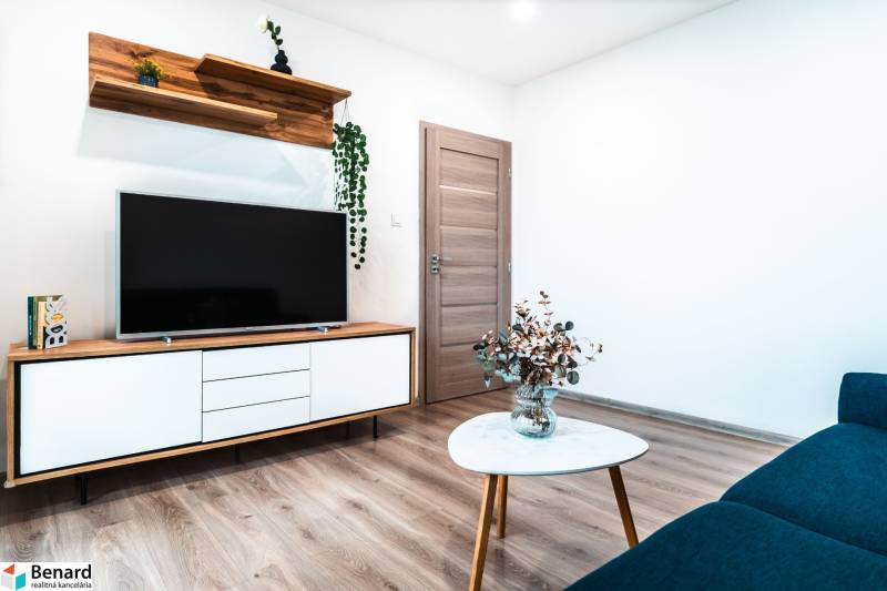 Útulný 2-izbový byt na prenájom - Obývacia izba s televízorom, skriňou, stolčekom a podlahou s dreveným dekorom v 2-izbovom byte.