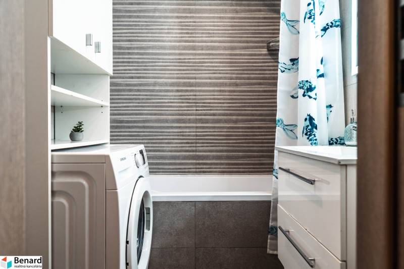 Útulný 2-izbový byt na prenájom - Kúpeľňa v 2-izbovom byte so sprchovým závesom, práčkou a úložným priestorom.