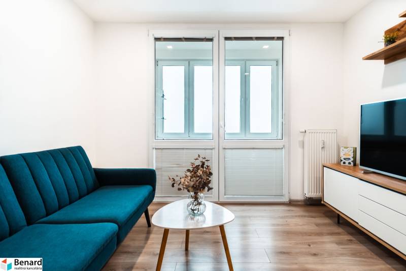 Útulný 2-izbový byt na prenájom - Obývacia izba v 2-izbovom byte so sedačkou, televízorom a podlahou s dreveným dekorom.