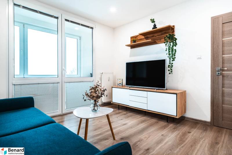 Útulný 2-izbový byt na prenájom - Obývacia izba v 2-izbovom byte so sedačkou, televízorom a podlahou s dreveným dekorom.