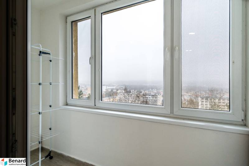 Útulný 2-izbový byt na prenájom - Balkón s výhľadom v 2-izbovom byte, stojan na prádlo, mesto v hmle.