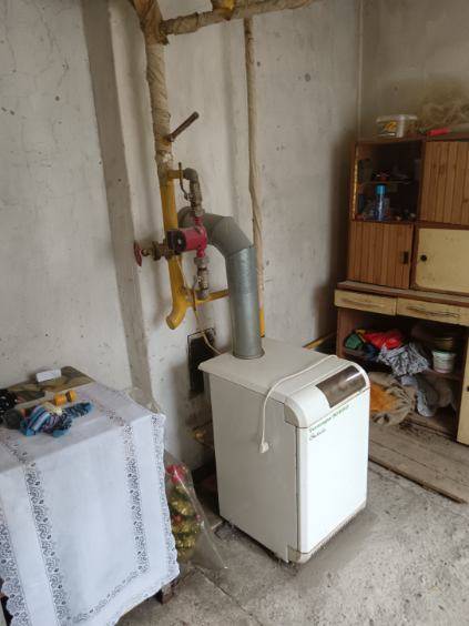 Na predaj rodinný dom Kosihovce - V rodinnom dome sa nachádza kotol vedľa drevenej police a rúr na stene.