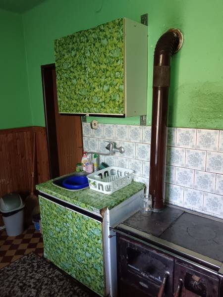 Na predaj rodinný dom Kosihovce - Staršia kuchyňa v rodinnom dome s kachľami, umývadlom a dekoratívnym obložením.