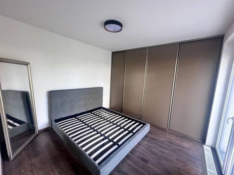 Na prenájom 2iz. byt s predzáhradkou  - Spálňa v 2-izbovom byte s posteľou, zrkadlom a skriňou, podlaha s dreveným dekorom.