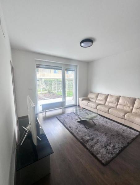 Na prenájom 2iz. byt s predzáhradkou  - Obývacia izba v 2-izbovom byte s veľkou pohovkou a podlahou s dreveným dekorom.