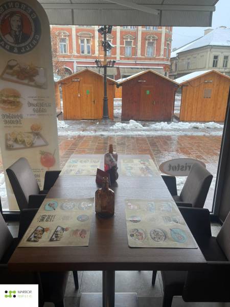 Reštaurácia na predaj v centre Košíc na Hlavnej 74 - Zimná scenéria cez okno gastro priestoru s pohľadom na drevené stolíky.