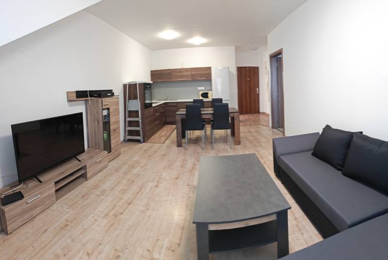 Prenájom 3-izbový byt v Malackách - Obývacia izba v 3-izbovom byte s podlahou s dreveným dekorom, kuchynským kútom a sedačkou.