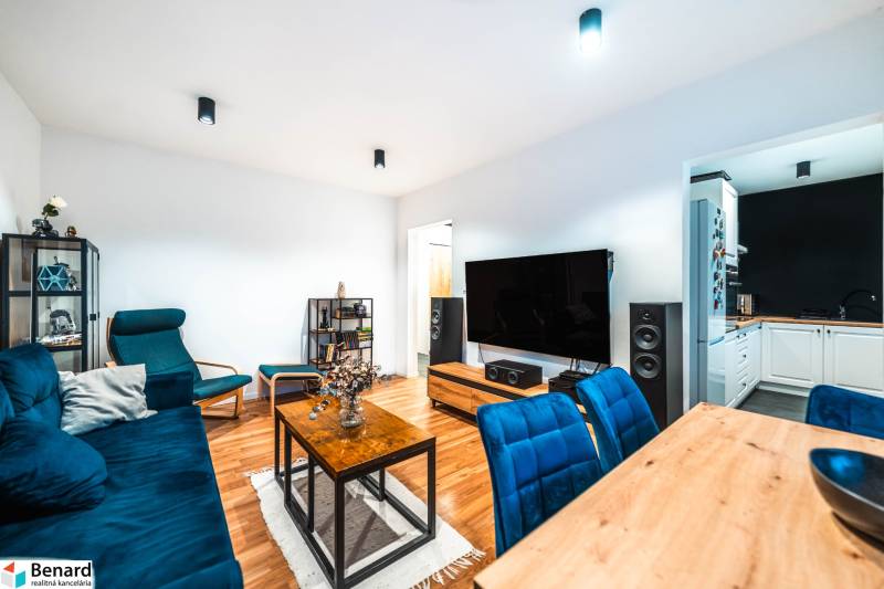 Na prenájom moderný 2-izbový byt  - Obývacia izba 2-izbového bytu s podlahou s dreveným dekorom a modrými sedacimi súpravami.