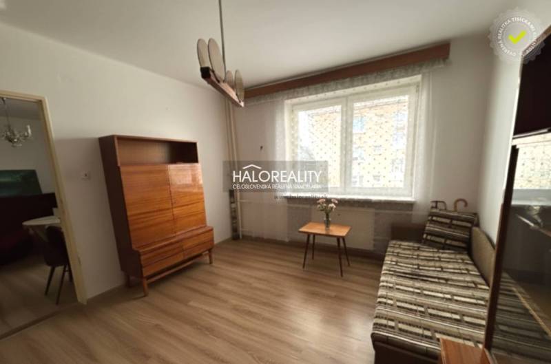 Predaj, trojizbový byt Spišské Vlachy - Obývacia izba v 3-izbovom byte s podlahou s dreveným dekorom, sedačkou, skrinkou a oknom.