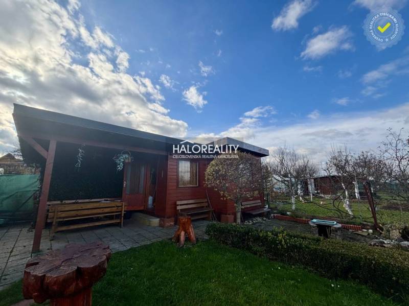 Predaj, záhradný pozemok   231 m2 Spišská Nová Ves, ... - Drevená chatka v záhradách Spišskej Novej Vsi s lavičkami a kvetinovým záhonom.