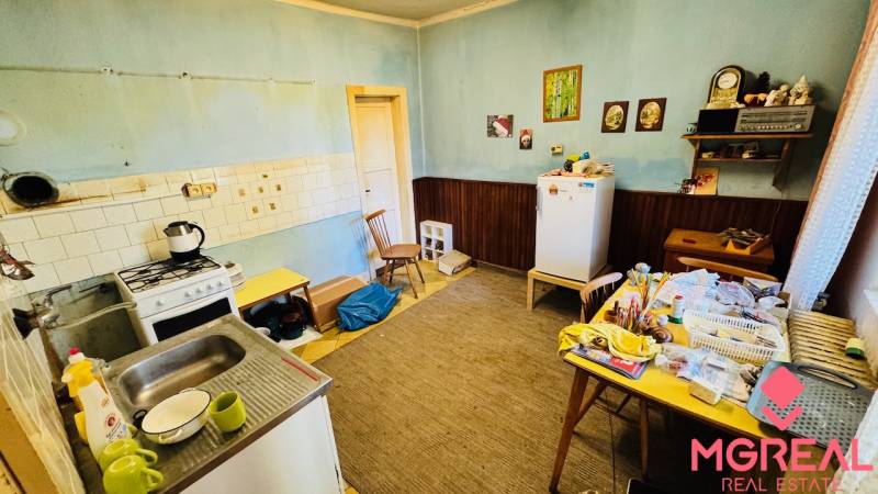 Na predaj 4-izbový rodinný dom v Brodzanoch – pozemok 1236 m² - Kuchyňa v rodinnom dome s jedálenským stolom, starším sporákom a chladničkou.