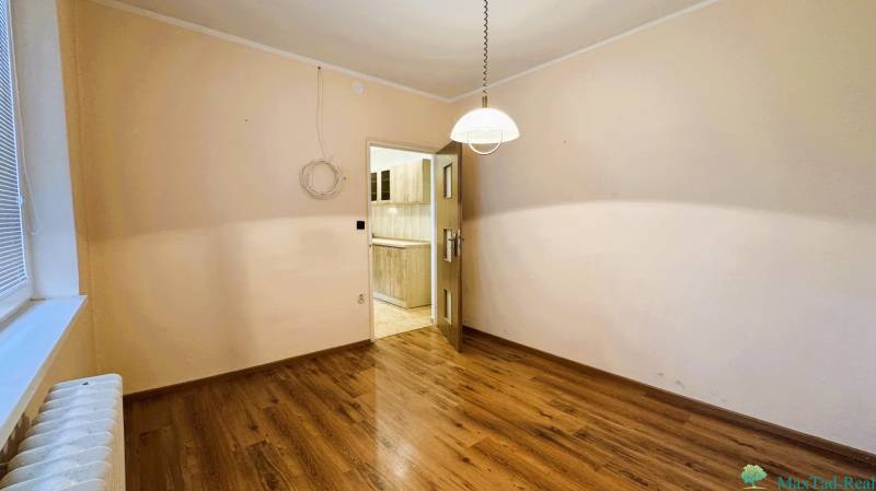 Výborná poloha, skvelá dispozícia – 3-izbový byt v Trebišove - Izba v 3-izbovom byte s podlahou s dreveným dekorom, pohľad do kuchyne.