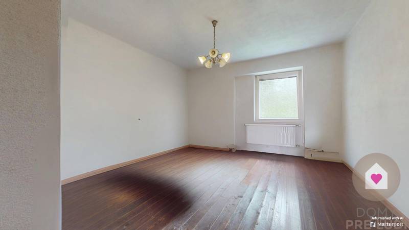 Veľký priestranný pozemok o rozlohe 7445 m2, Jelka  - Prázdna izba s drevenou podlahou a lustrom v rodinnom dome.
