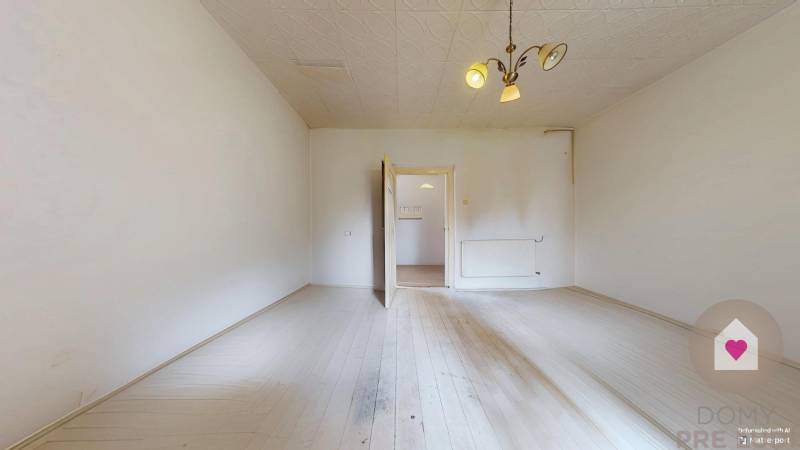 Veľký priestranný pozemok o rozlohe 7445 m2, Jelka  - Priestranná miestnosť s bielou podlahou, radiátorom a lustrom v rodinnom dome.